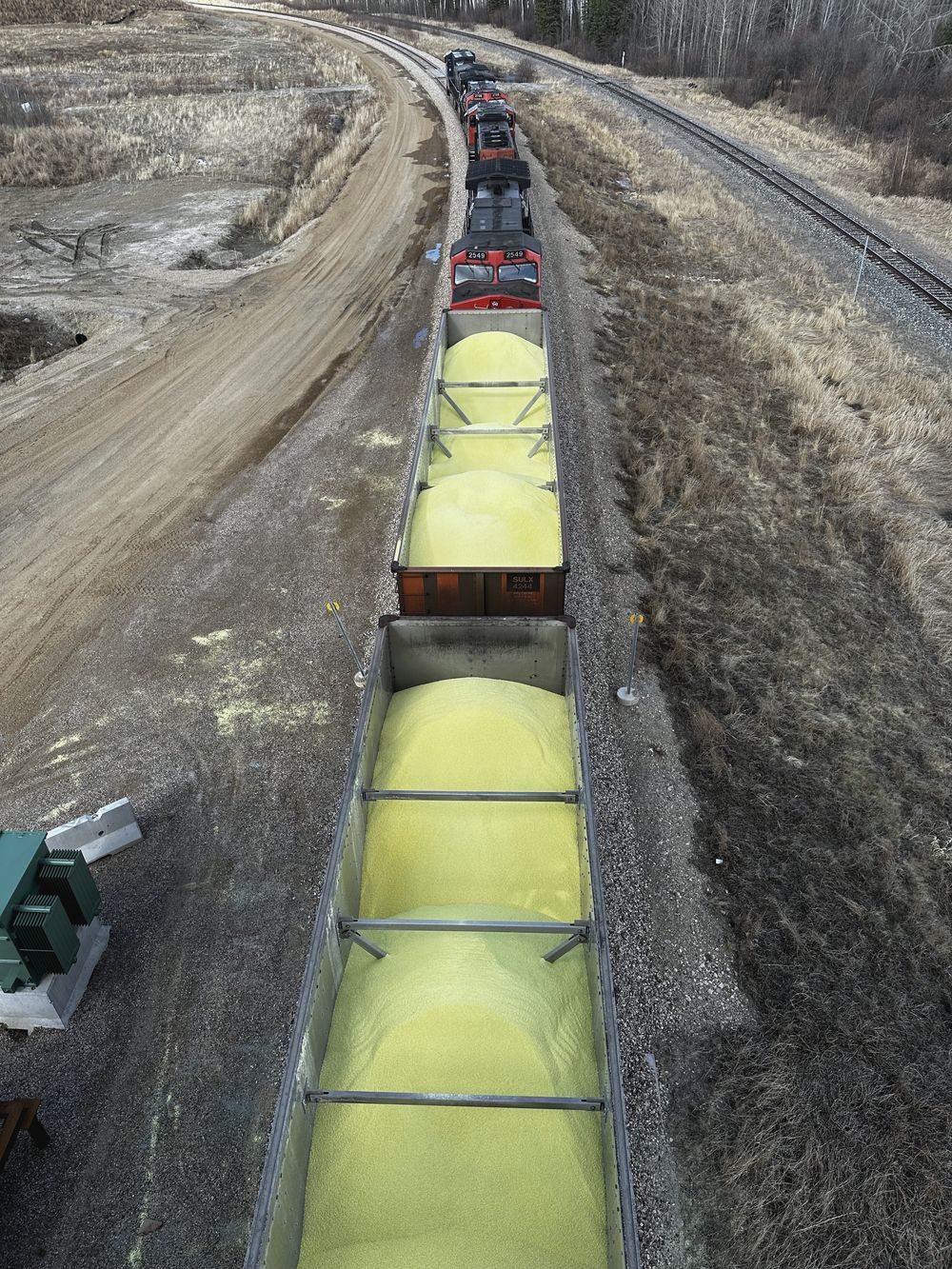 Loaded hopper cars curving through a rail-served terminal, seen from above