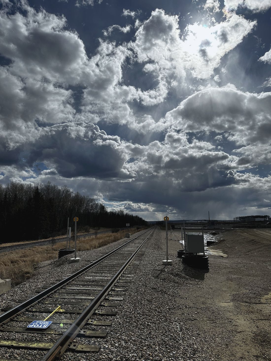 Rail line and loaded cars under towering prairie clouds